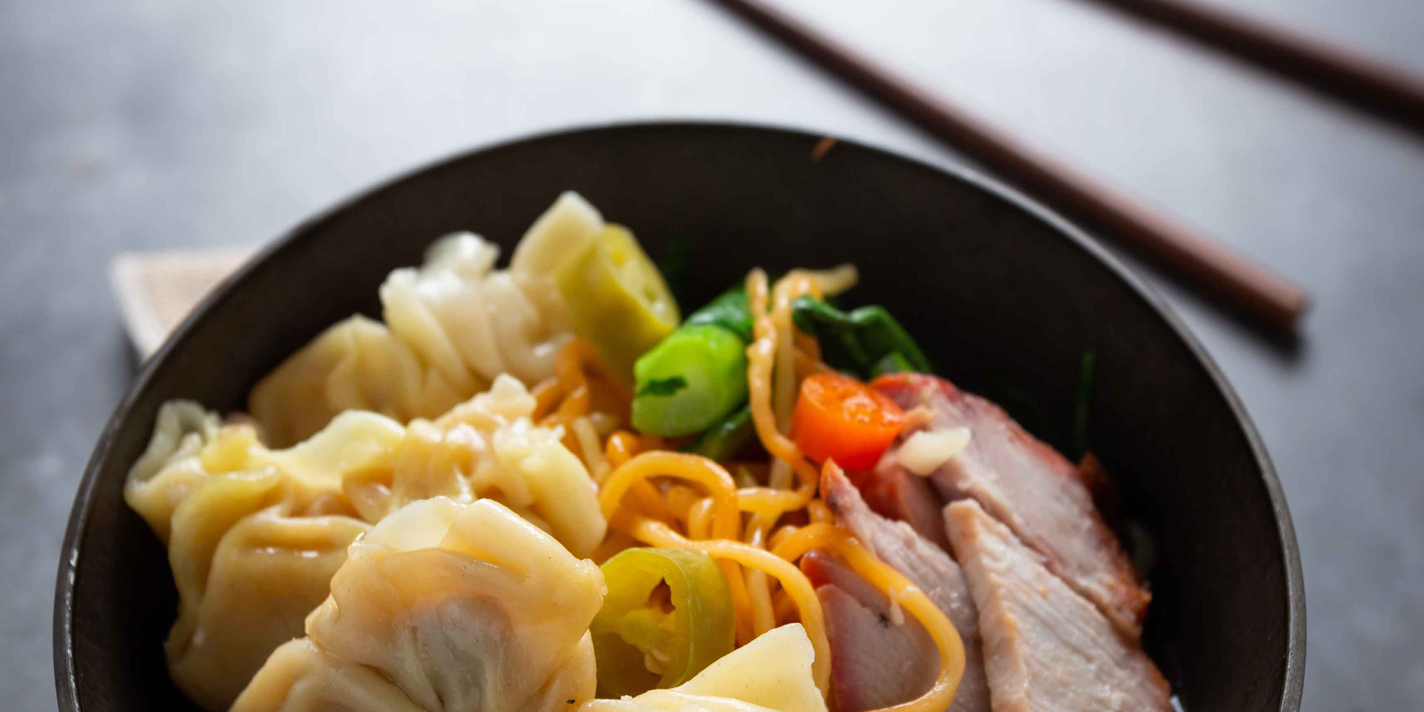 Egg noodle with red roasted pork and wonton on table.